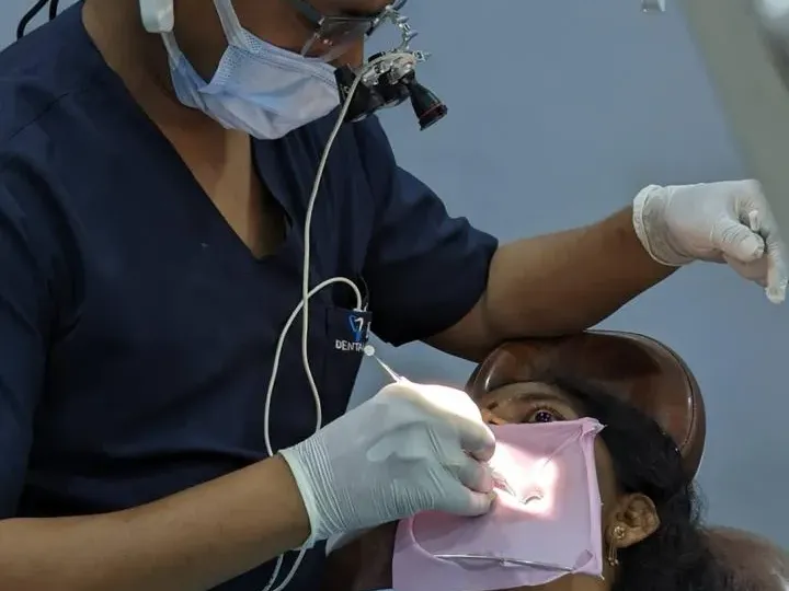 Dr. Konagala Ravi Kumar, MDS endodontist, treating a tooth under magnification loupes with rubber dam isolation, MVP Colony Vizag
